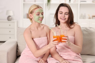 Photo of Spa day. Beautiful women with face masks and healthy drinks on sofa indoors