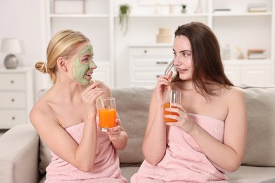 Photo of Spa day. Beautiful women with face masks and healthy drinks on sofa indoors