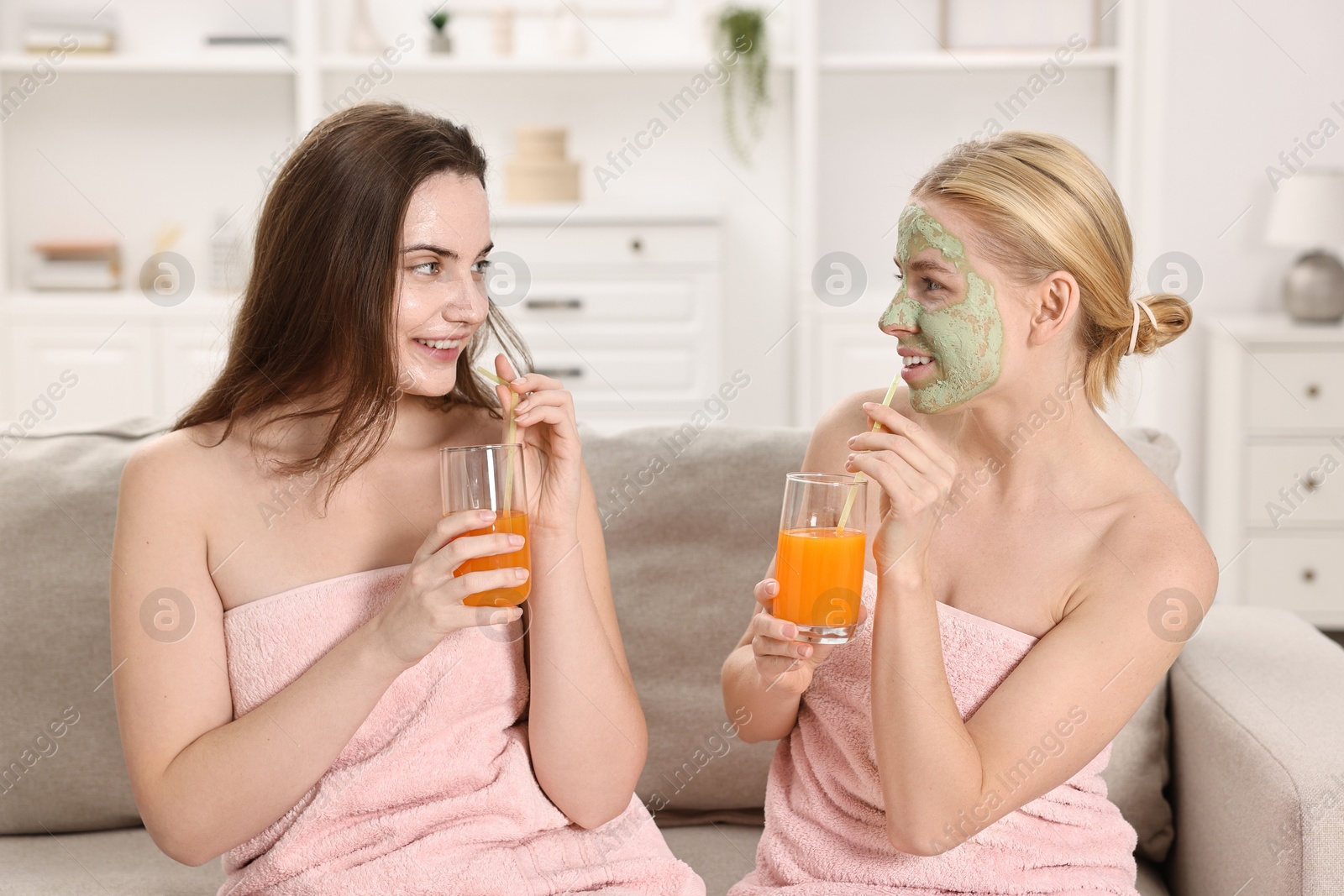 Photo of Spa day. Beautiful women with face masks and healthy drinks on sofa indoors