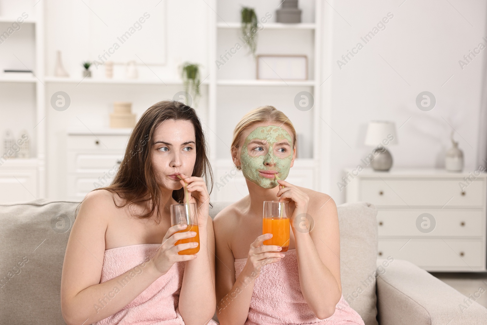 Photo of Spa day. Beautiful women with face masks and healthy drinks on sofa indoors