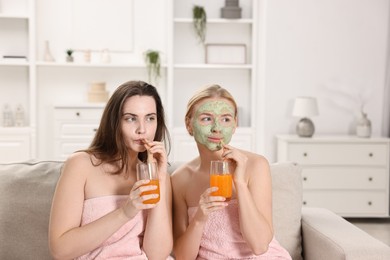 Spa day. Beautiful women with face masks and healthy drinks on sofa indoors