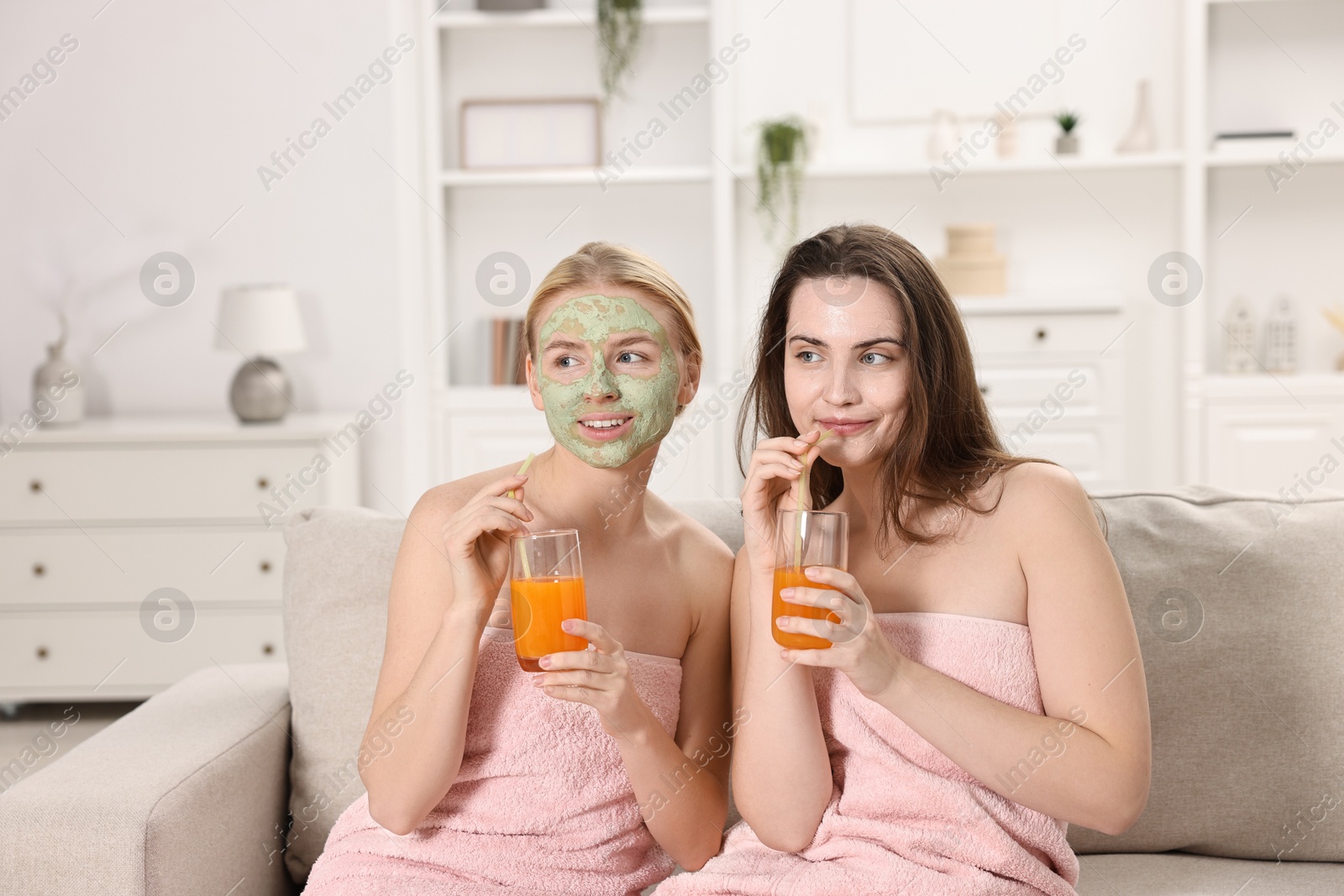 Photo of Spa day. Beautiful women with face masks and healthy drinks on sofa indoors