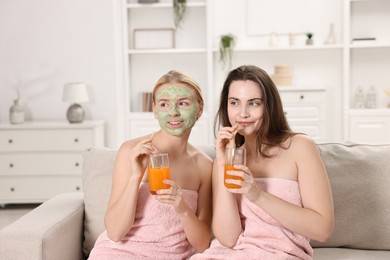 Photo of Spa day. Beautiful women with face masks and healthy drinks on sofa indoors