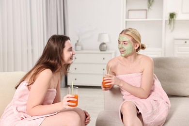 Spa day. Beautiful women with face masks and healthy drinks on sofa indoors