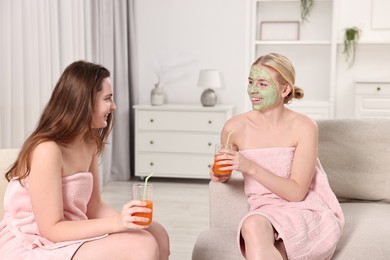 Photo of Spa day. Beautiful women with face masks and healthy drinks on sofa indoors