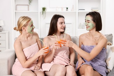 Photo of Spa day. Beautiful women with face masks and healthy drinks on sofa indoors