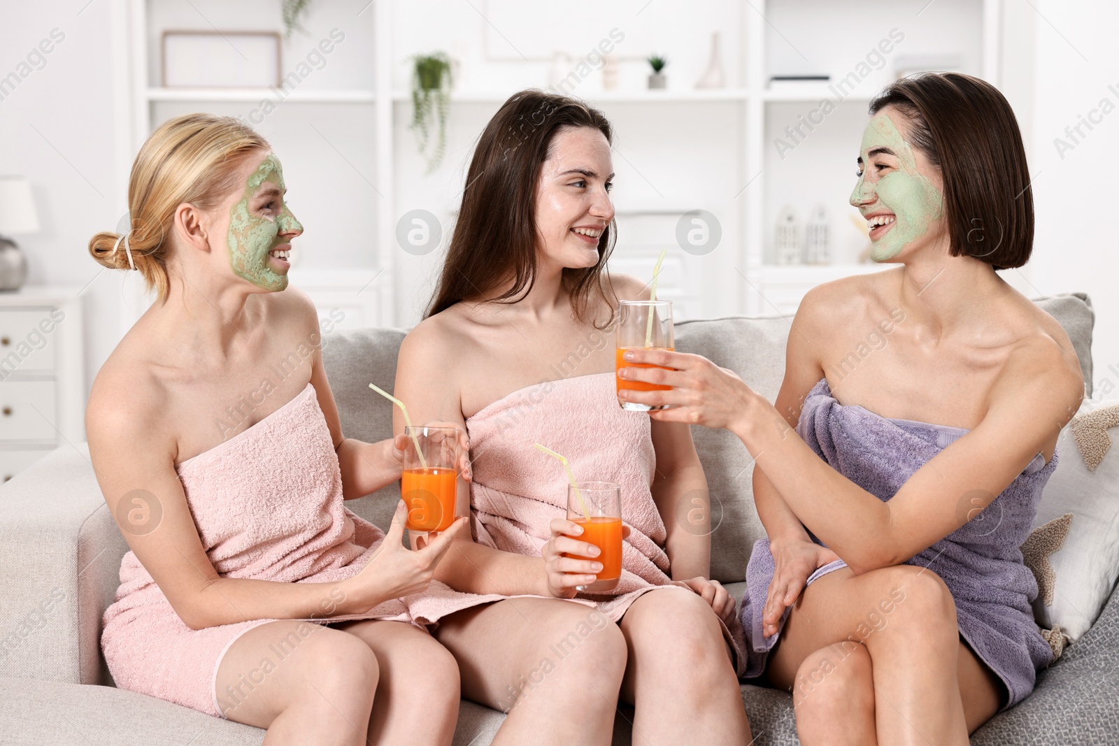 Photo of Spa day. Beautiful women with face masks and healthy drinks on sofa indoors