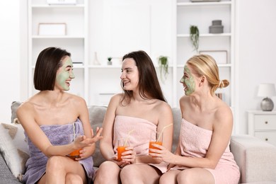 Photo of Spa day. Beautiful women with face masks and healthy drinks on sofa indoors