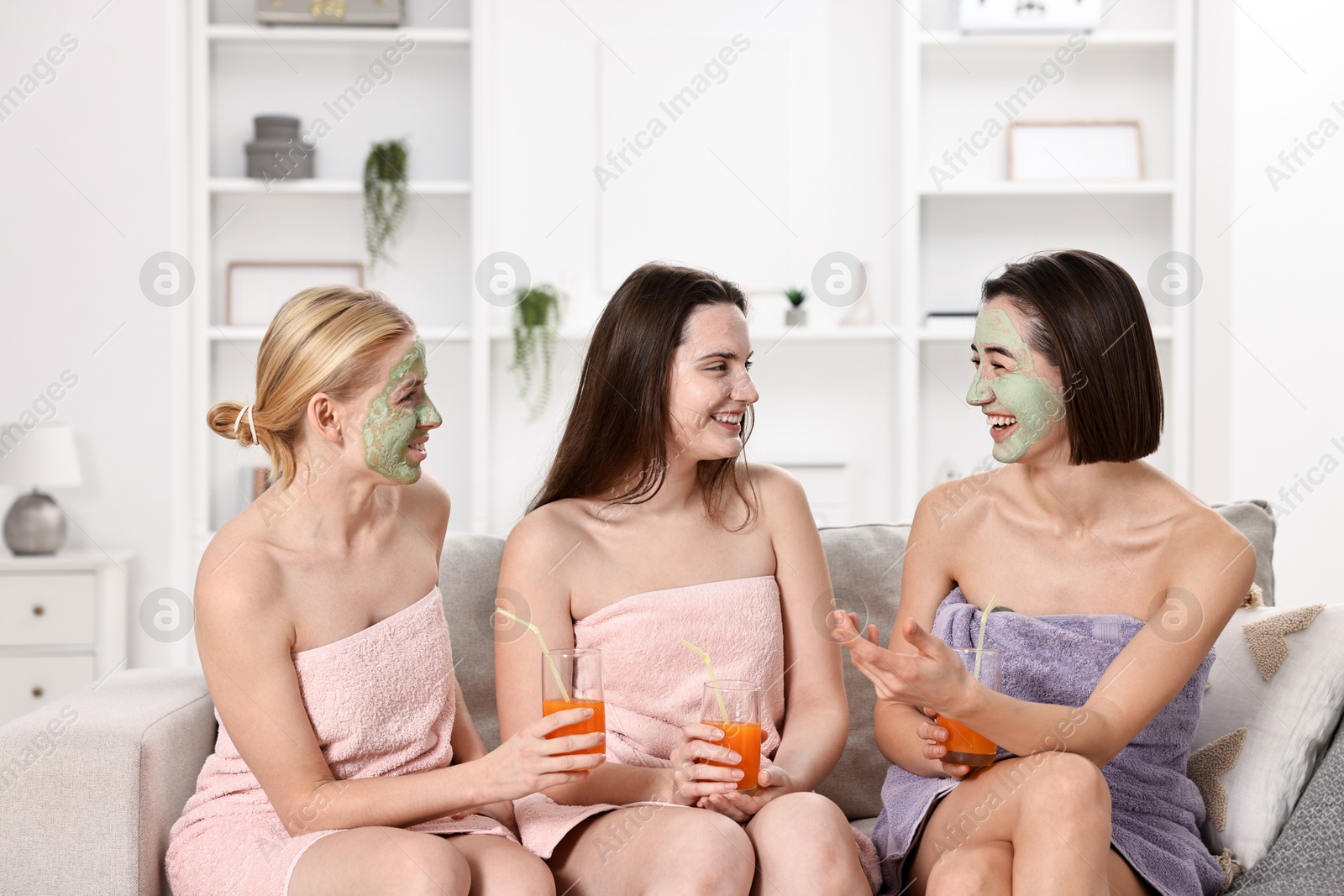 Photo of Spa day. Beautiful women with face masks and healthy drinks on sofa indoors