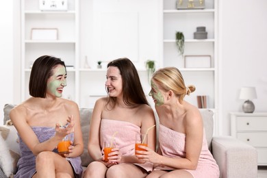 Photo of Spa day. Beautiful women with face masks and healthy drinks on sofa indoors