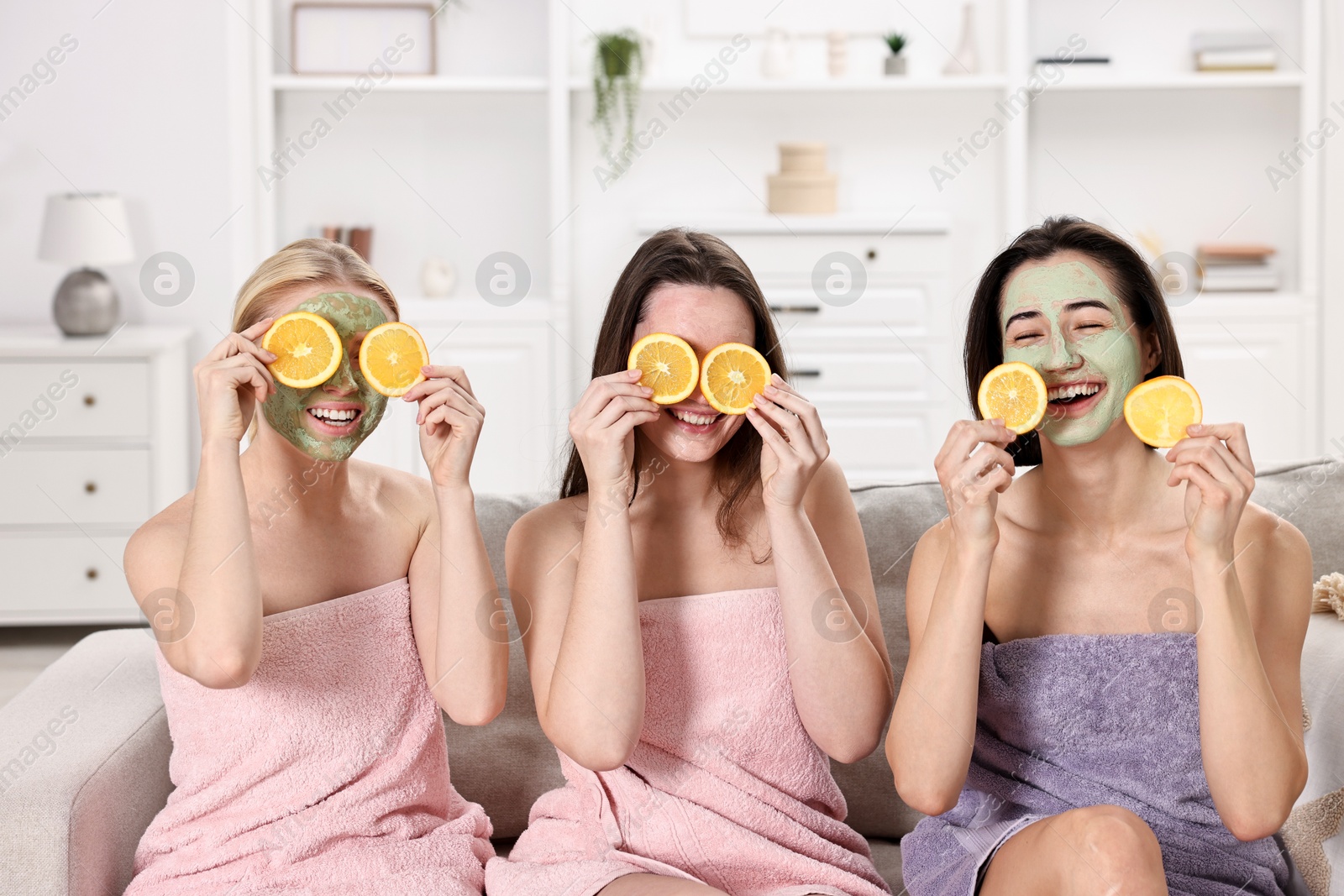 Photo of Spa day. Beautiful women with face masks and orange slices on sofa indoors