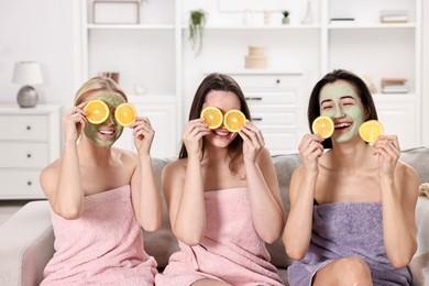 Photo of Spa day. Beautiful women with face masks and orange slices on sofa indoors