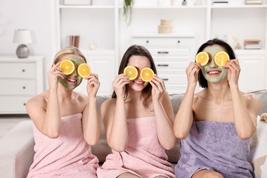 Photo of Spa day. Beautiful women with face masks and orange slices on sofa indoors