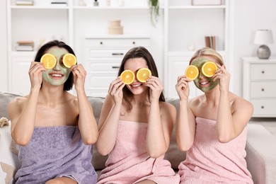 Photo of Spa day. Beautiful women with face masks and orange slices on sofa indoors