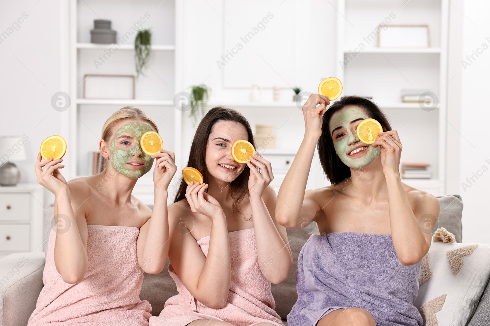 Photo of Spa day. Beautiful women with face masks and orange slices on sofa indoors