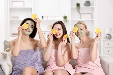 Photo of Spa day. Beautiful women with face masks and orange slices on sofa indoors