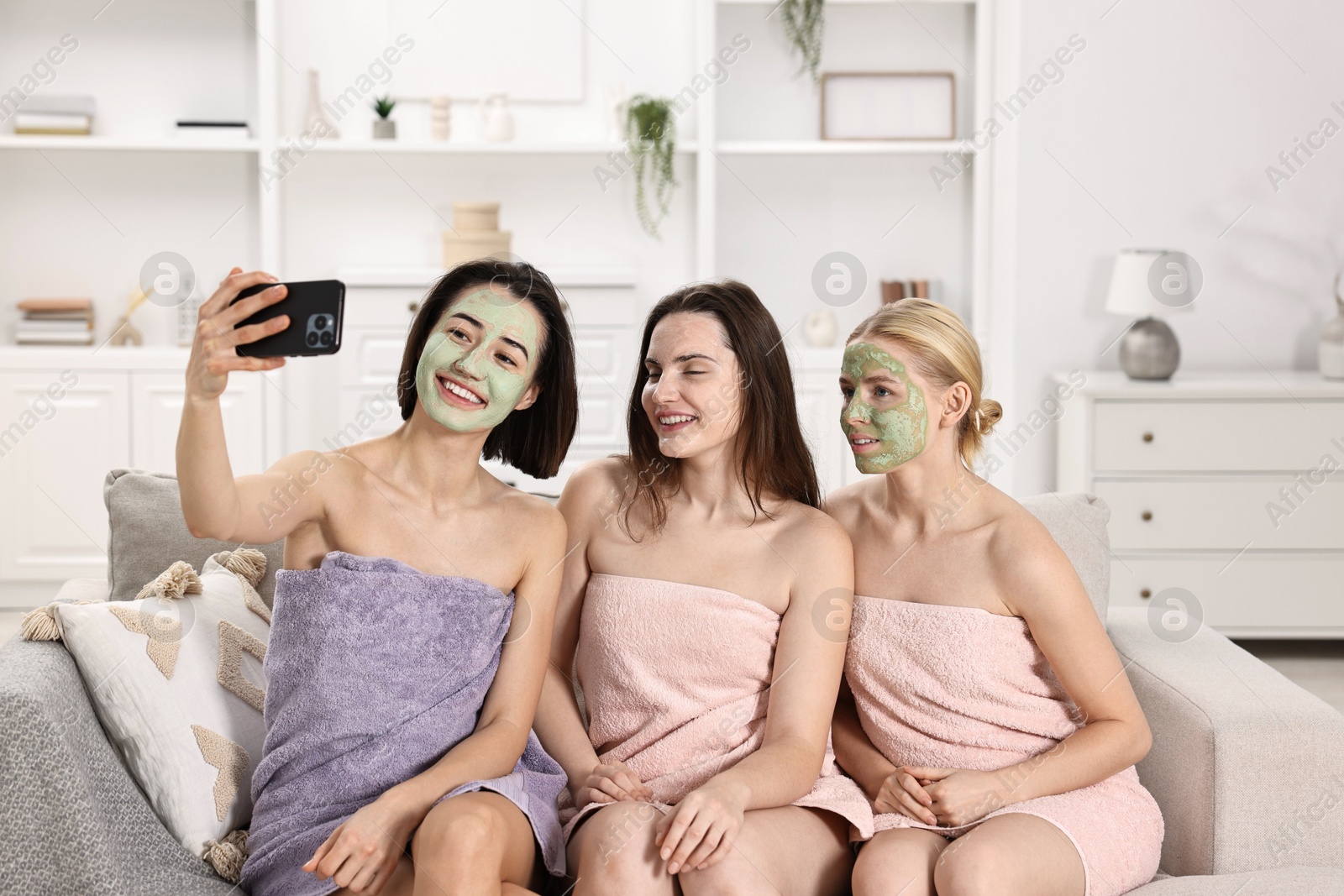 Photo of Spa day. Beautiful women with face masks taking selfie on sofa indoors