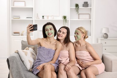 Photo of Spa day. Beautiful women with face masks taking selfie on sofa indoors