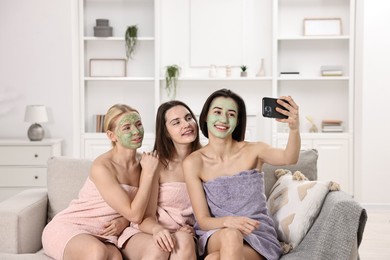 Photo of Spa day. Beautiful women with face masks taking selfie on sofa indoors