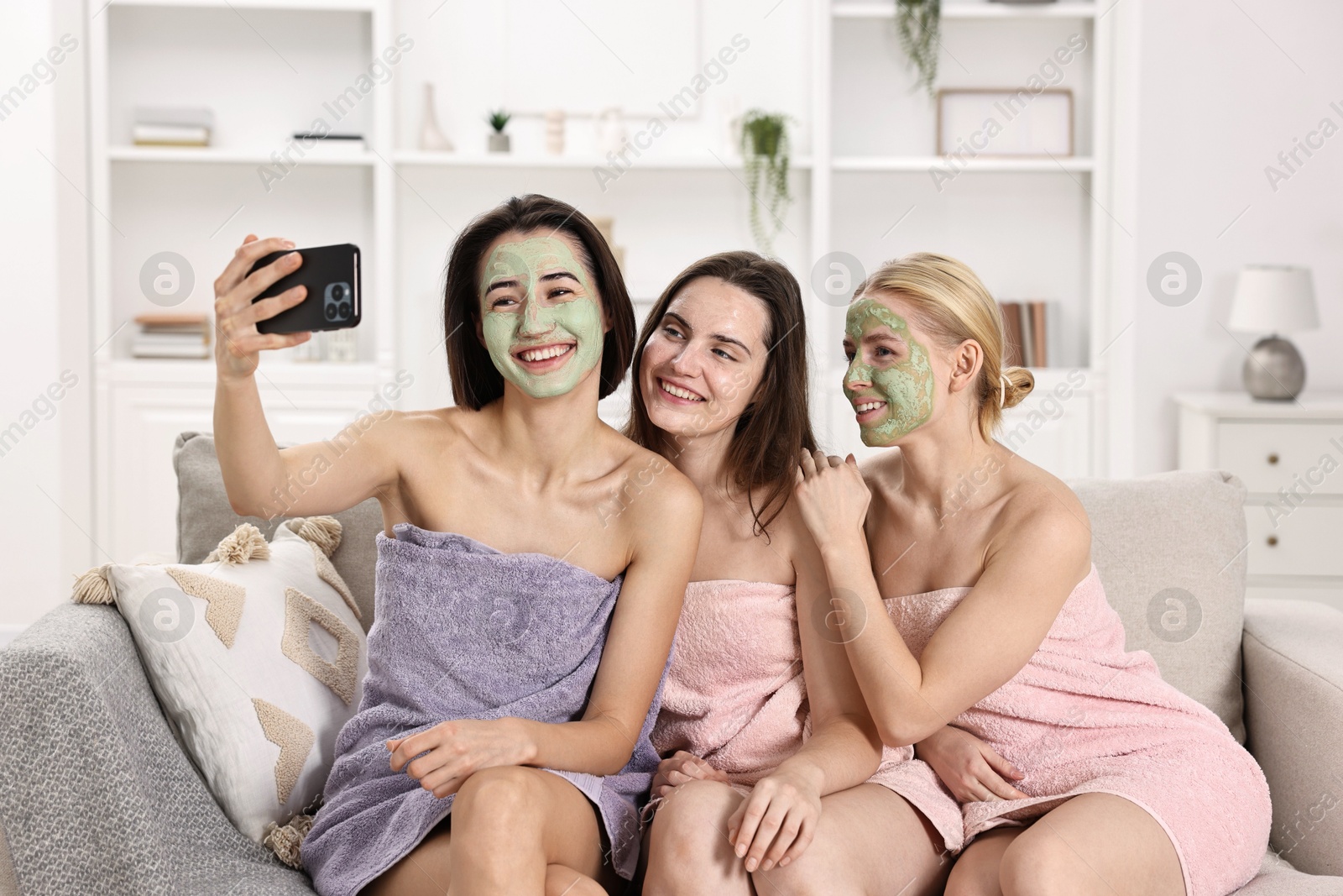 Photo of Spa day. Beautiful women with face masks taking selfie on sofa indoors