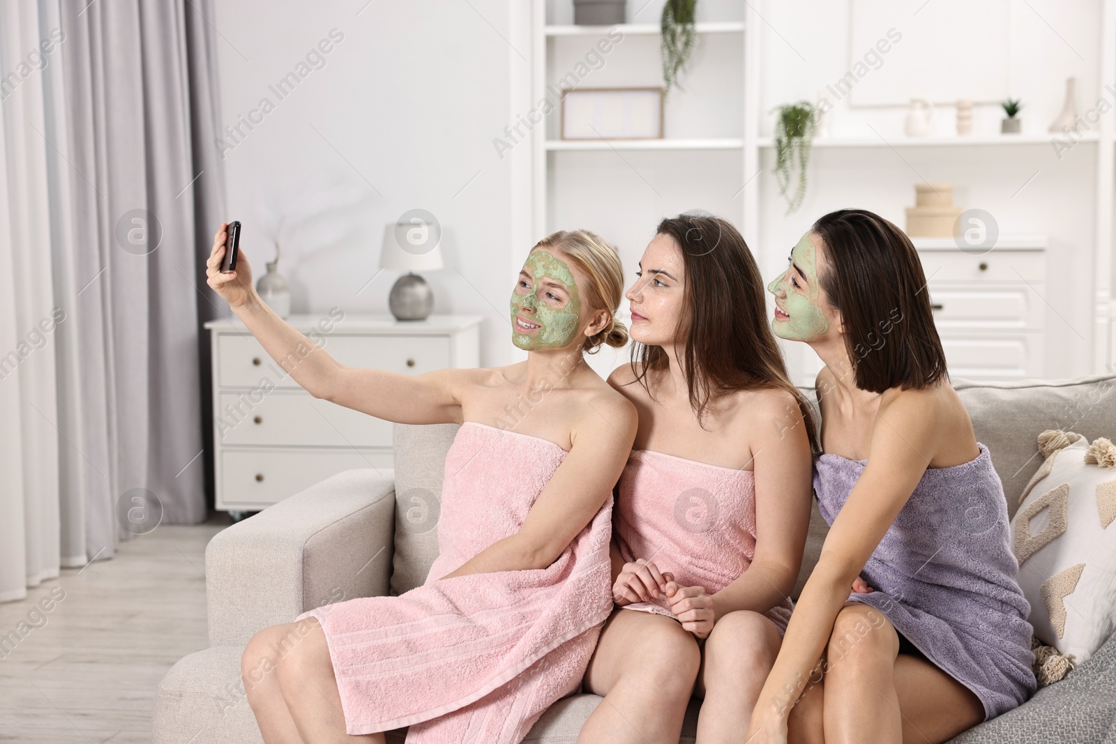 Photo of Spa day. Beautiful women with face masks taking selfie on sofa indoors