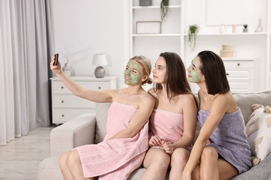 Photo of Spa day. Beautiful women with face masks taking selfie on sofa indoors