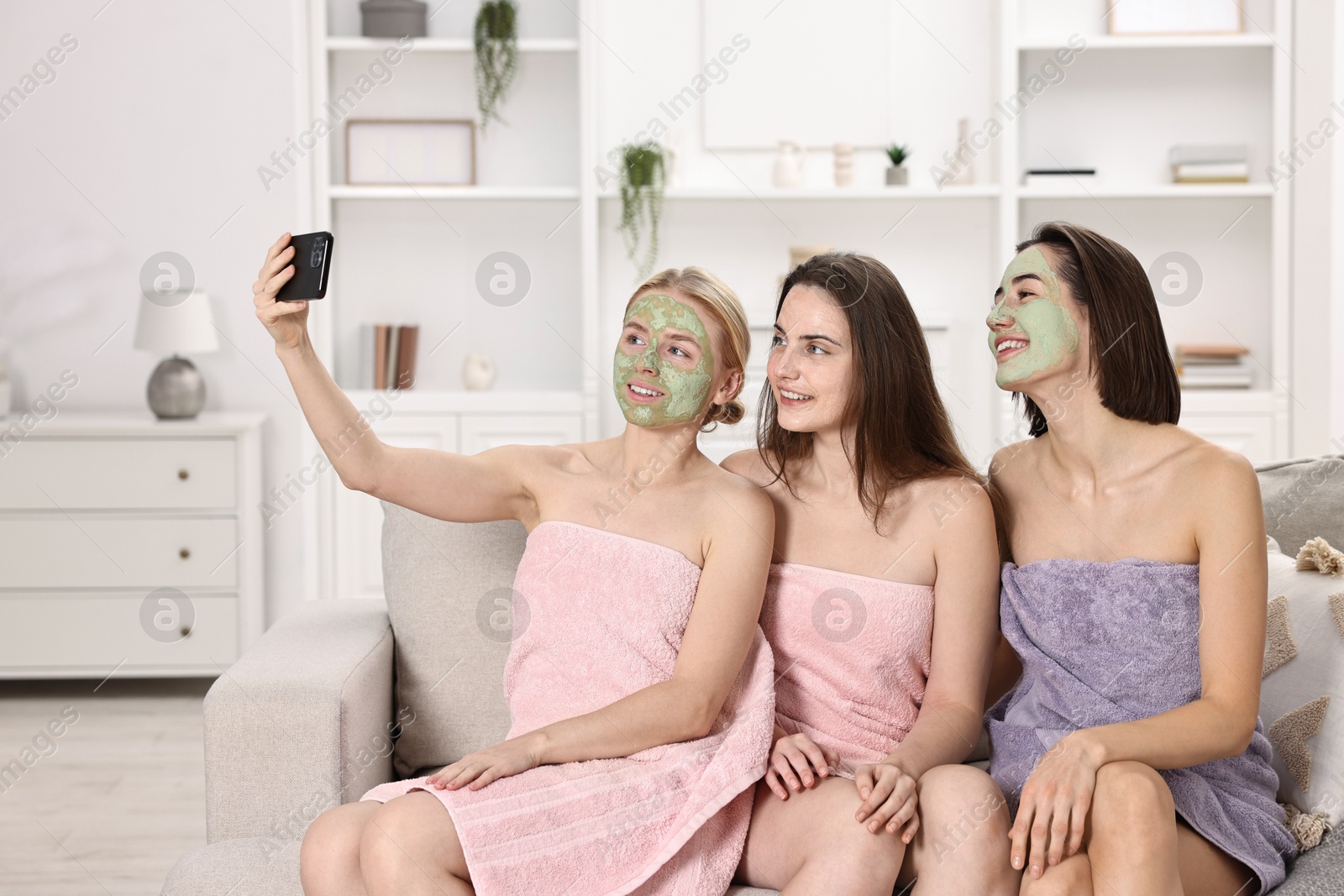 Photo of Spa day. Beautiful women with face masks taking selfie on sofa indoors