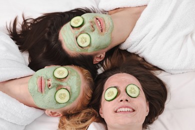 Photo of Spa day. Beautiful woman with face masks and cucumber slices on bed, above view