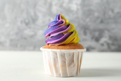 Photo of One delicious cupcake with colorful cream on white wooden table against blurred grey background, closeup