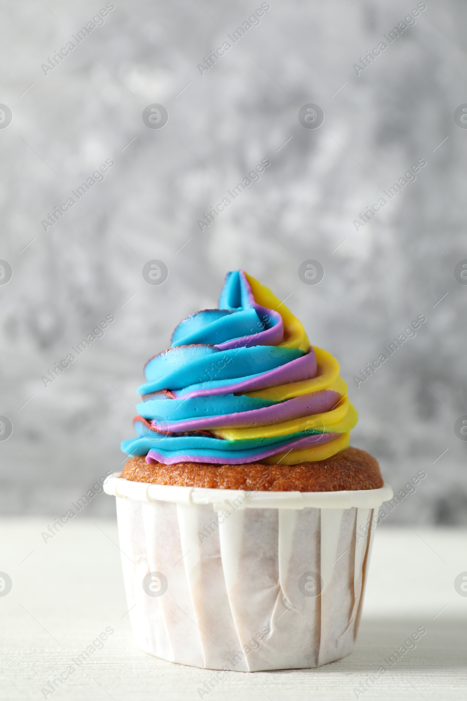 Photo of One delicious cupcake with colorful cream on white wooden table against blurred grey background, closeup