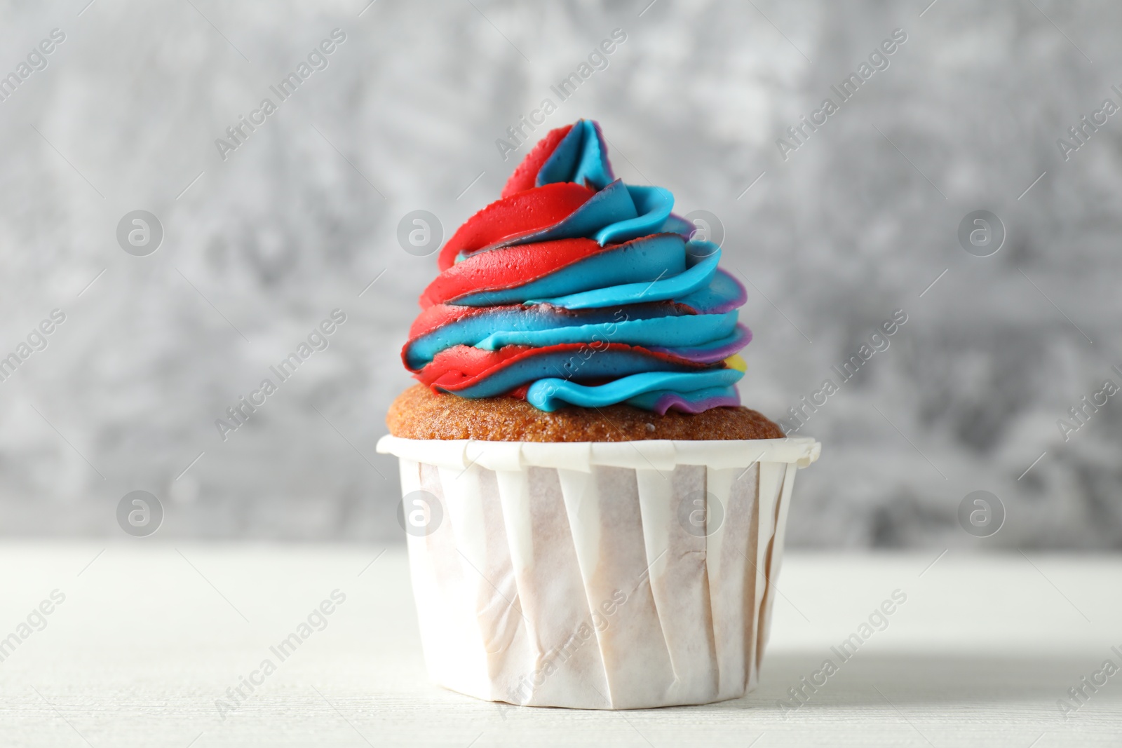 Photo of One delicious cupcake with colorful cream on white wooden table against blurred grey background, closeup