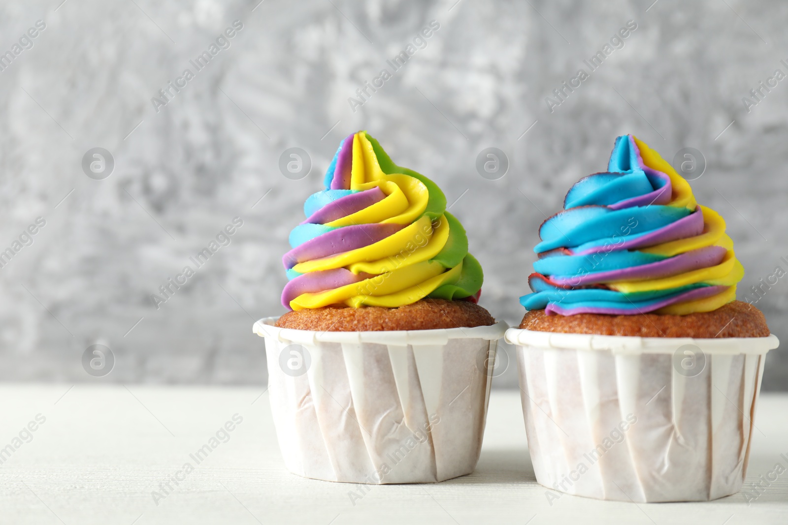 Photo of Delicious cupcakes with colorful cream on white wooden table against blurred grey background, closeup. Space for text