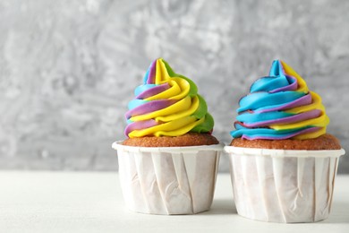 Photo of Delicious cupcakes with colorful cream on white wooden table against blurred grey background, closeup. Space for text