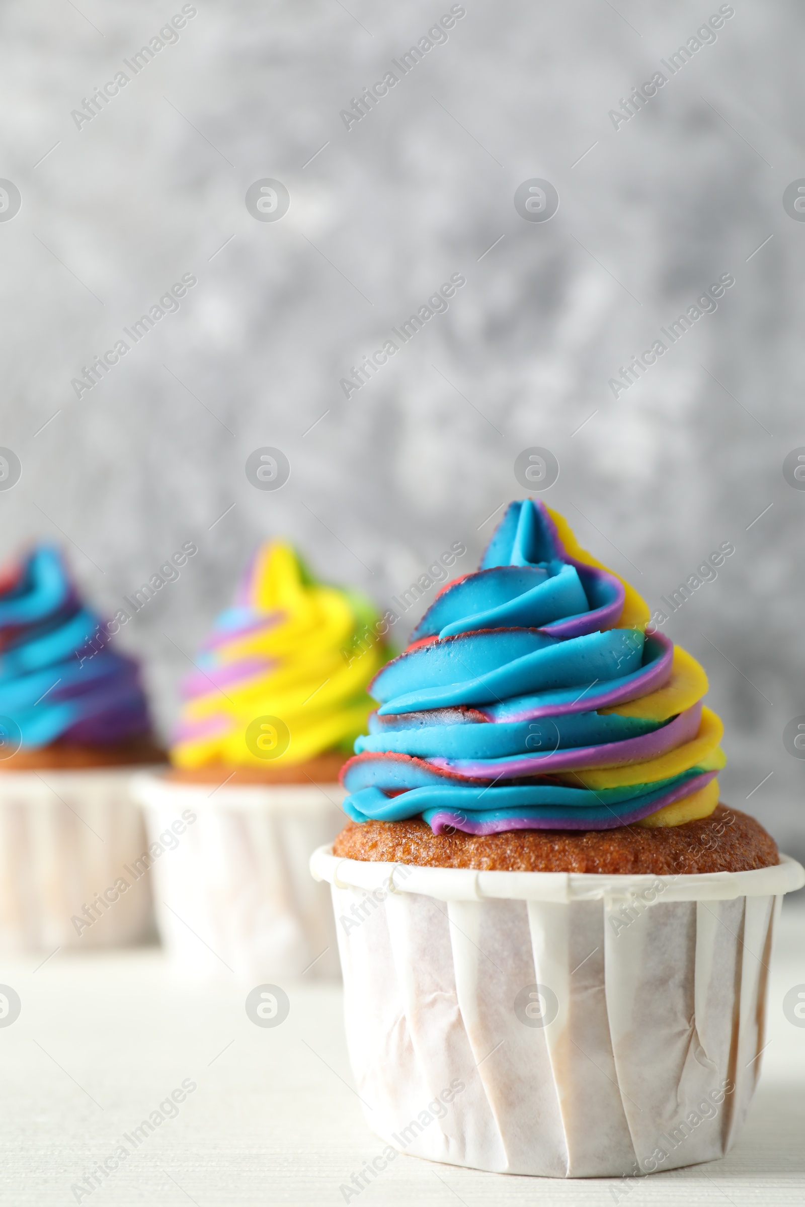 Photo of Delicious cupcakes with colorful cream on white wooden table against blurred grey background, closeup