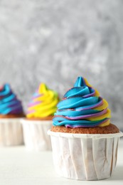 Photo of Delicious cupcakes with colorful cream on white wooden table against blurred grey background, closeup