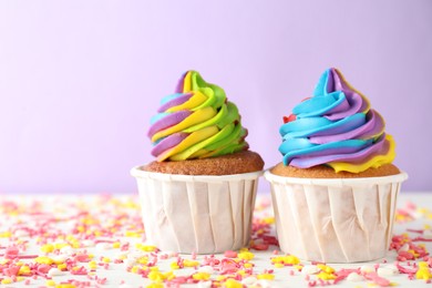 Photo of Delicious cupcakes with colorful cream and sprinkles on white wooden table against violet background, closeup. Space for text