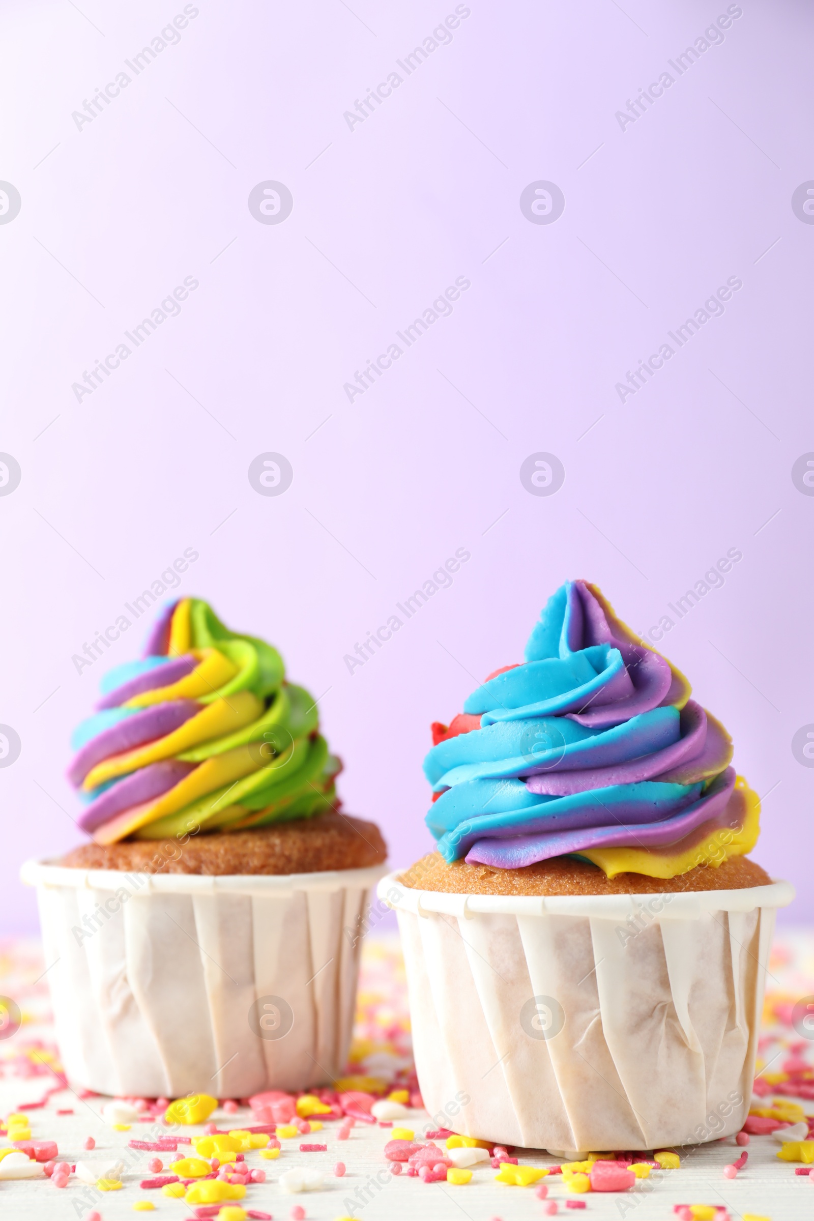 Photo of Delicious cupcakes with colorful cream and sprinkles on white wooden table against violet background, closeup. Space for text