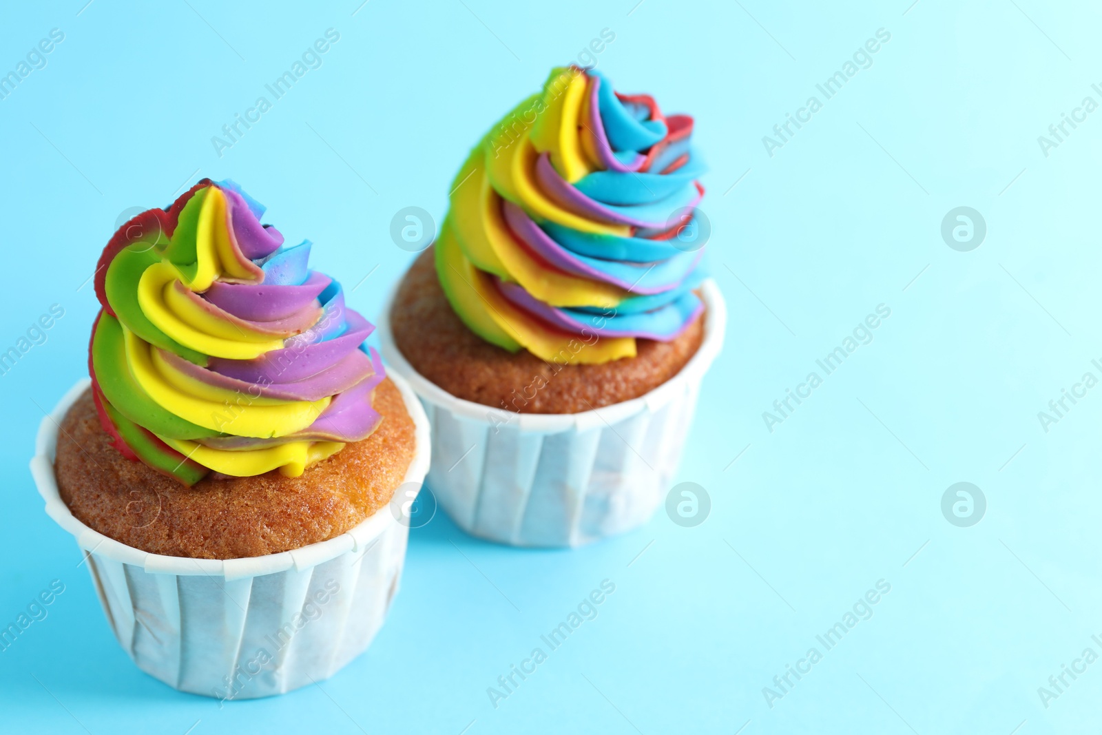 Photo of Delicious cupcakes with colorful cream on light blue background, closeup. Space for text