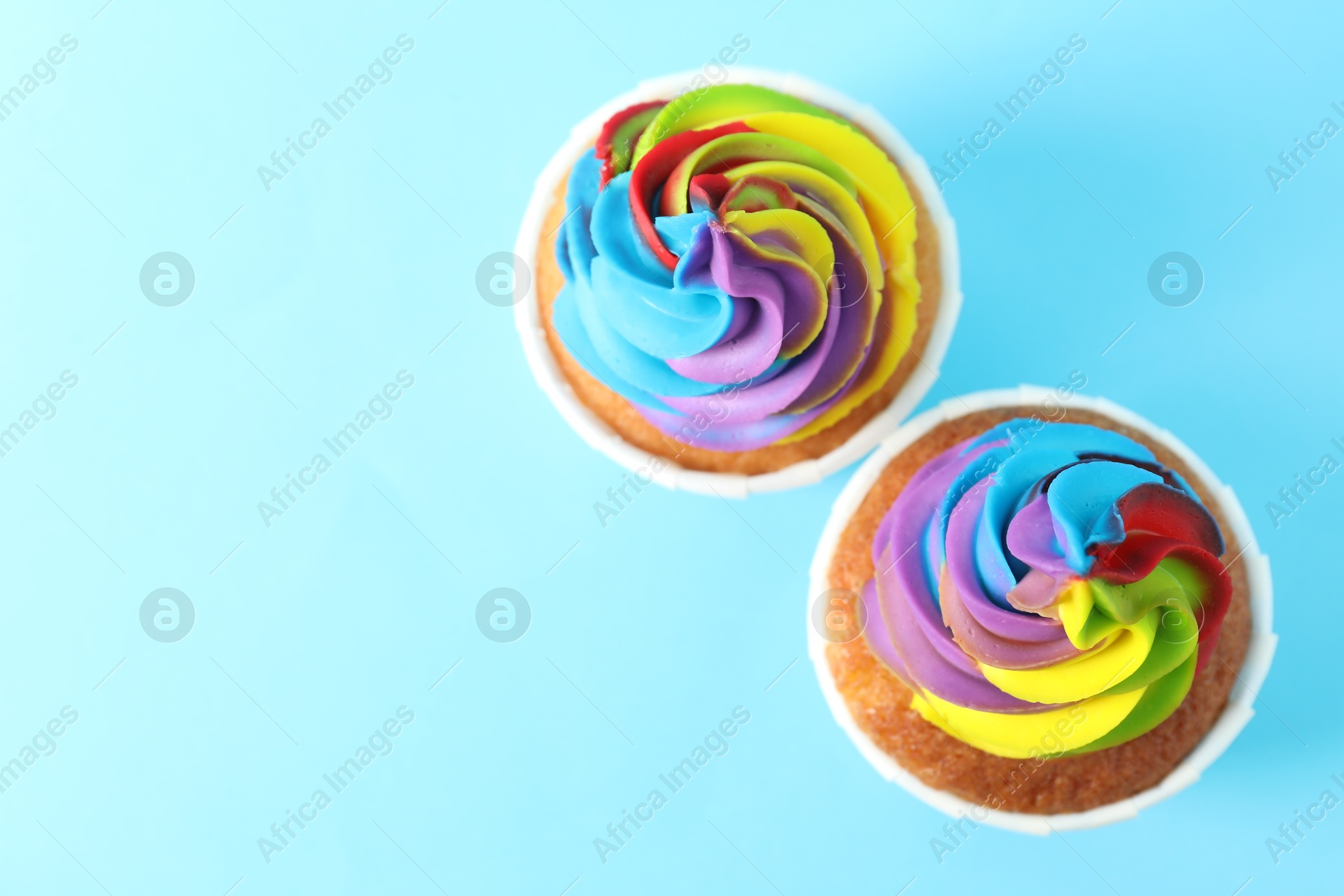 Photo of Delicious cupcakes with colorful cream on light blue background, flat lay. Space for text