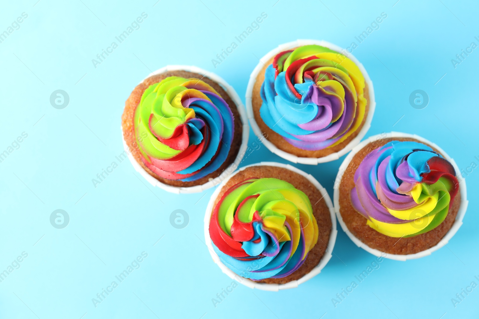 Photo of Delicious cupcakes with colorful cream on light blue background, flat lay. Space for text