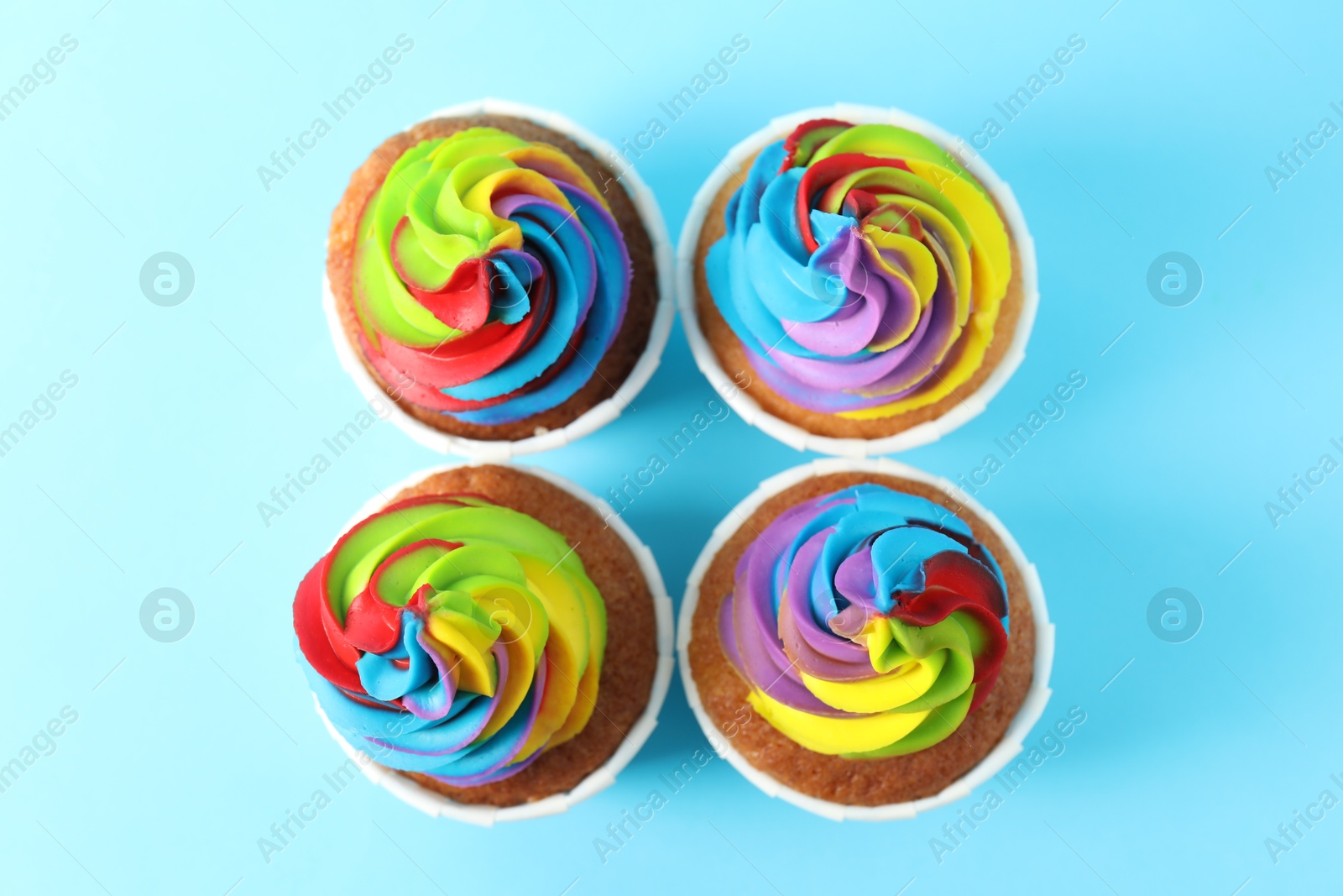 Photo of Delicious cupcakes with colorful cream on light blue background, flat lay