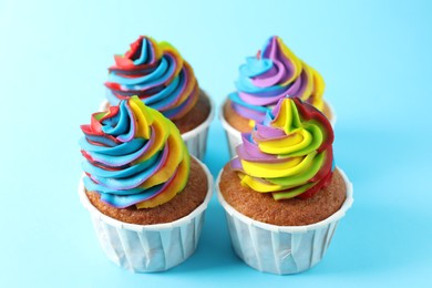 Photo of Delicious cupcakes with colorful cream on light blue background, closeup