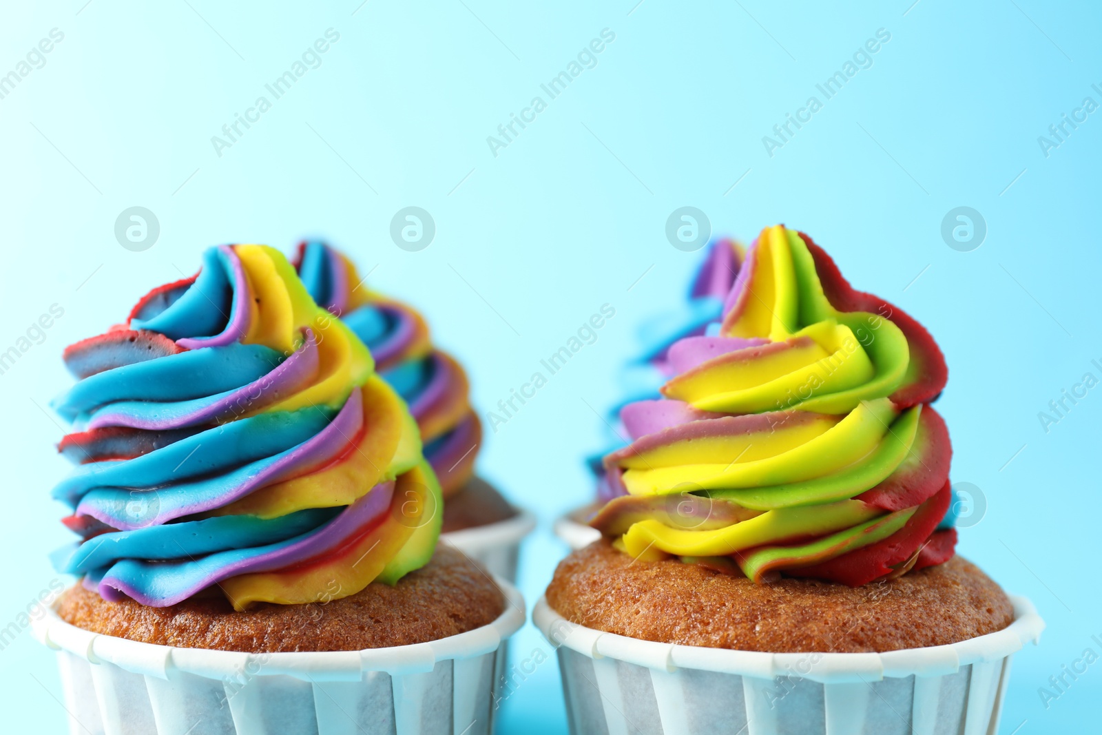 Photo of Delicious cupcakes with colorful cream on light blue background, closeup