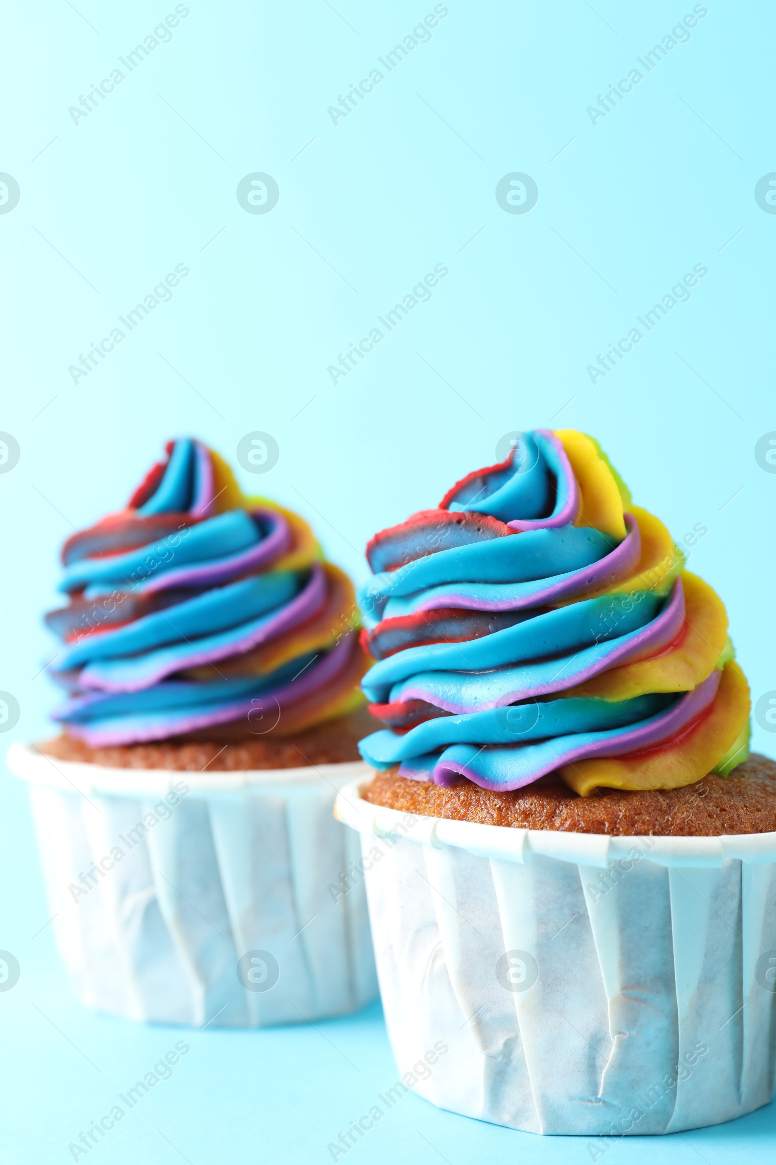 Photo of Delicious cupcakes with colorful cream on light blue background, closeup