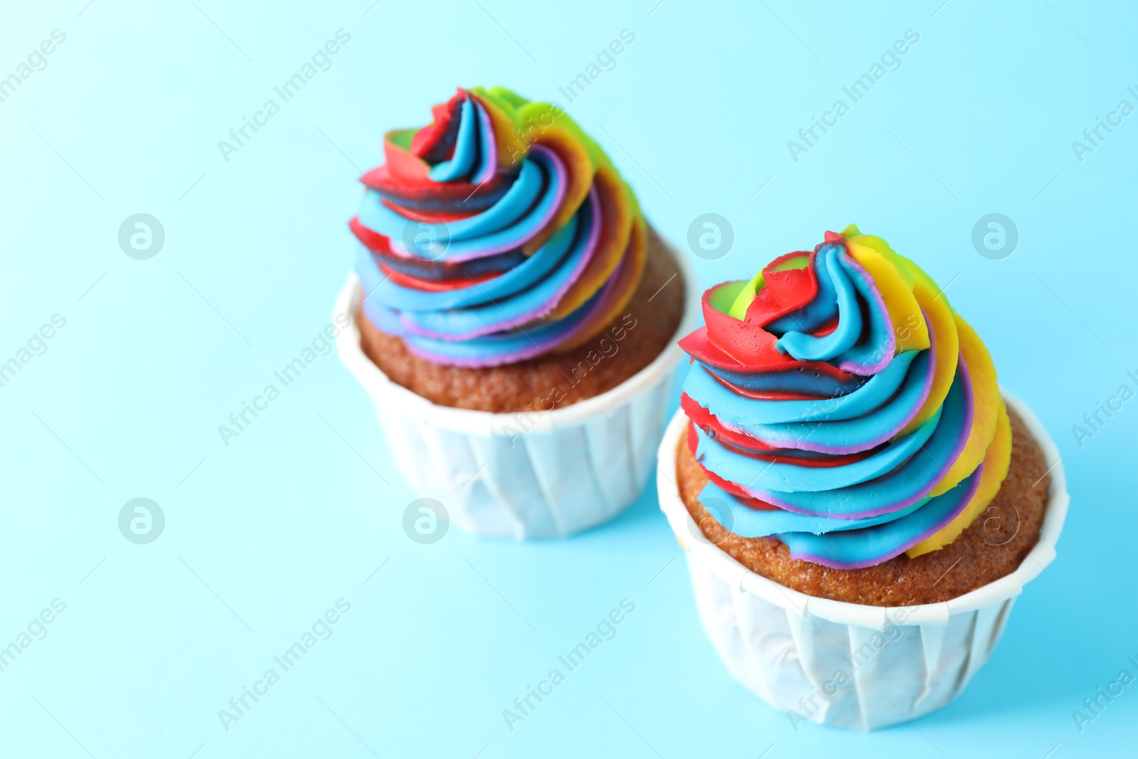 Photo of Delicious cupcakes with colorful cream on light blue background, closeup. Space for text