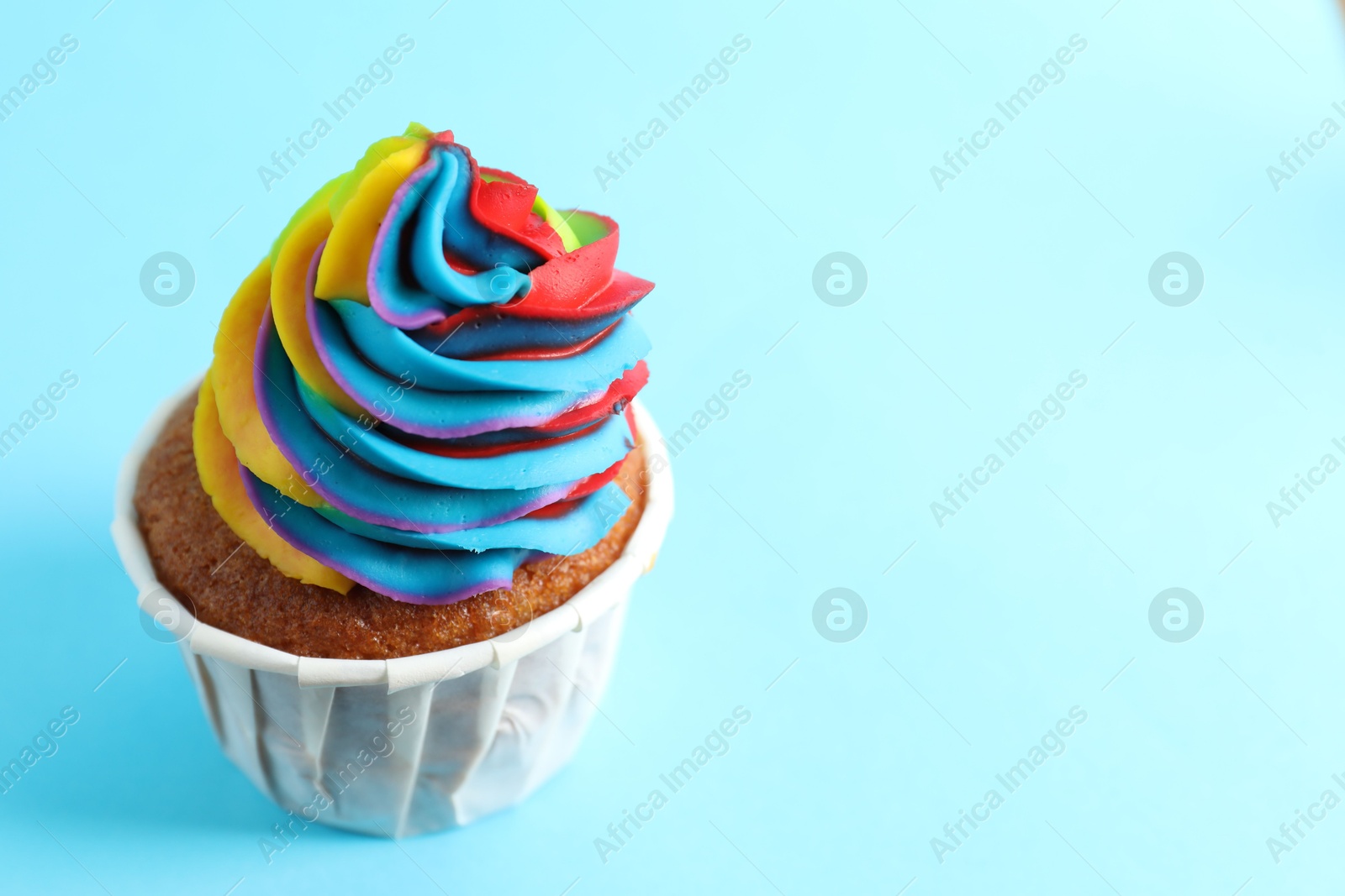 Photo of One delicious cupcake with colorful cream on light blue background, closeup. Space for text