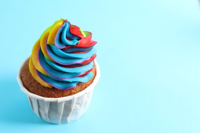 Photo of One delicious cupcake with colorful cream on light blue background, closeup. Space for text