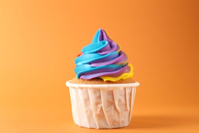 Photo of One delicious cupcake with colorful cream on orange background, closeup