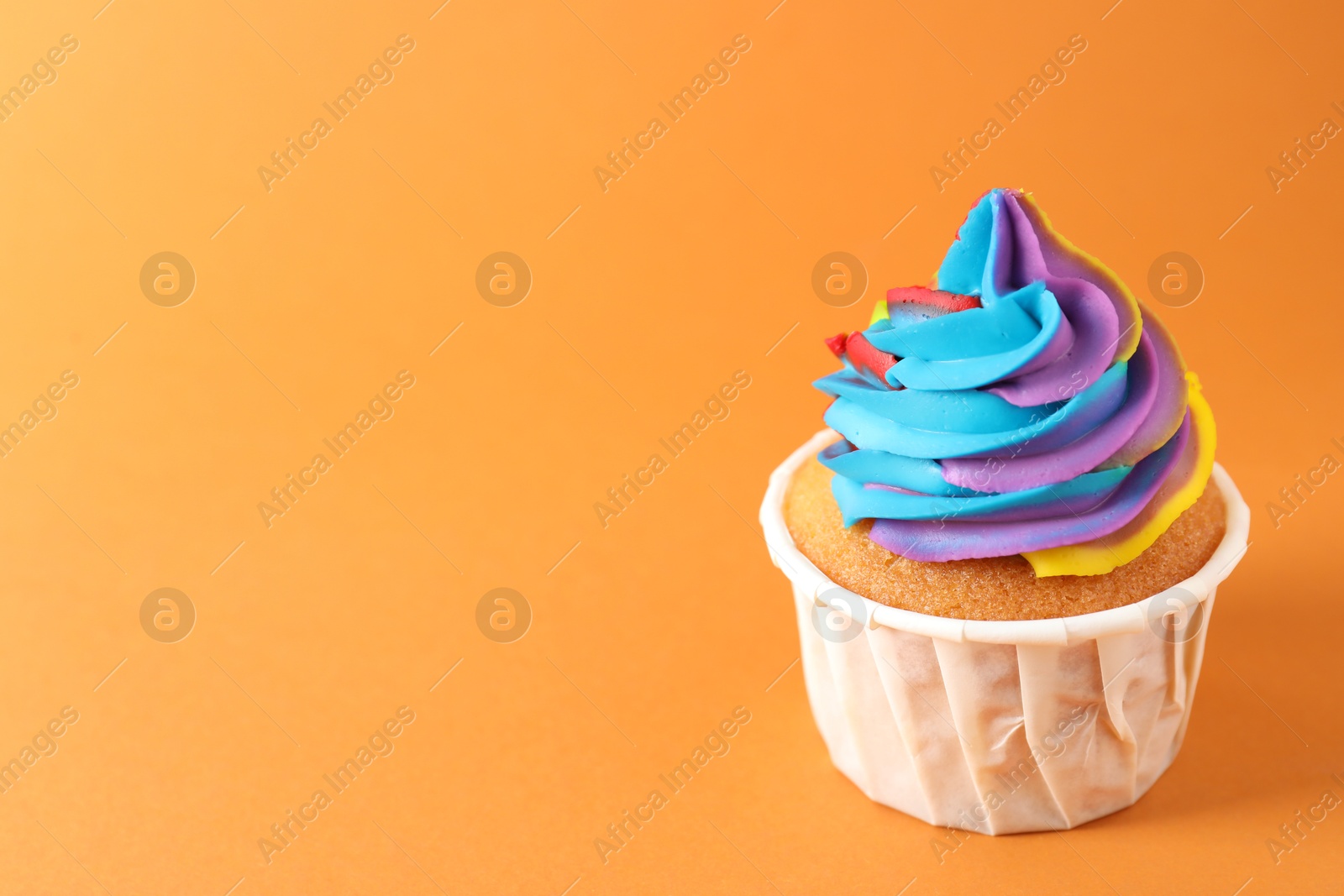 Photo of One delicious cupcake with colorful cream on orange background, closeup. Space for text