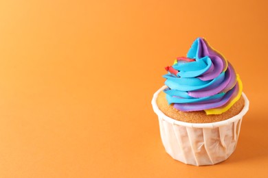 Photo of One delicious cupcake with colorful cream on orange background, closeup. Space for text